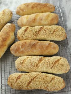 Several Sourdough Sub Rolls lined up on a cooling rack.
