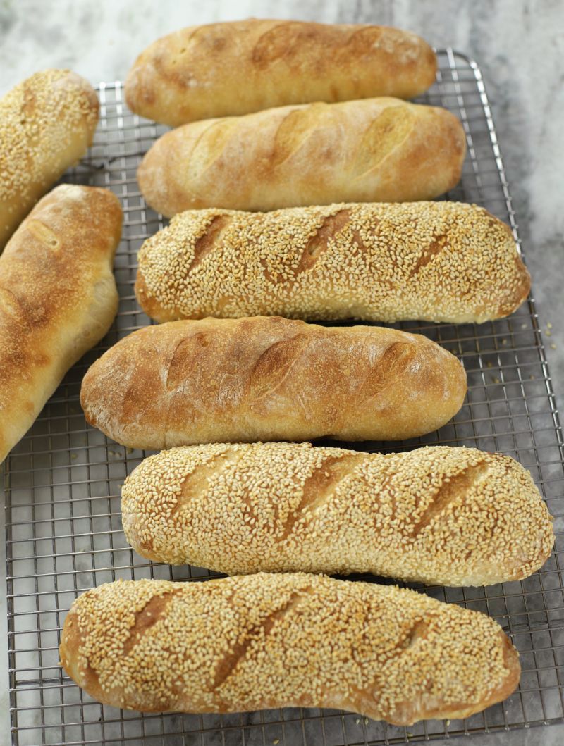 Several Sourdough Sub Rolls lined up on a cooling rack.