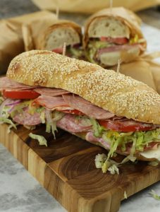 An Italian Sub Sandwich sitting on top of a wooden cutting board.