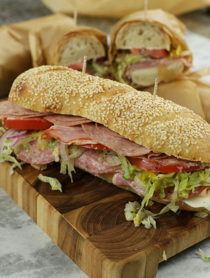 An Italian Sub Sandwich sitting on top of a wooden cutting board.
