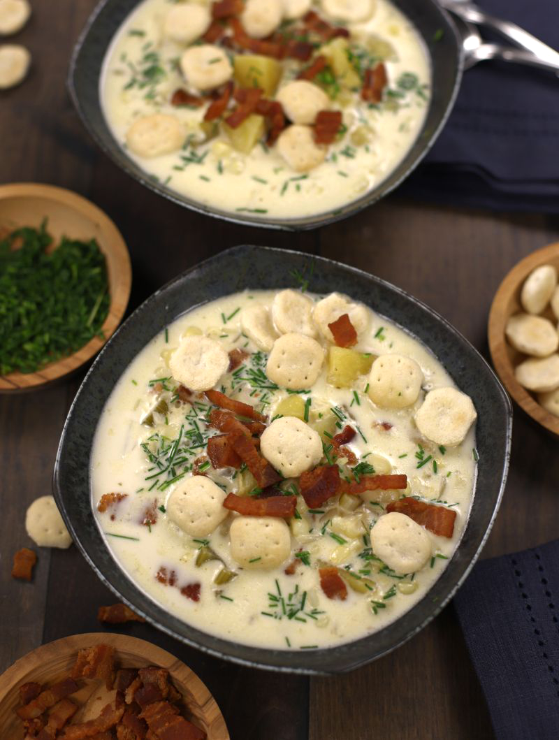 Overhead photo of Corn and Potato Chowder served in two dark grey bowls and garnished with oyster crackers.