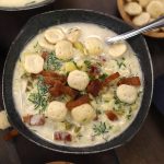A serving of Potato and Corn Soup garnished with fresh cut chives, crispy bacon strips and oyster crackers.