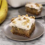 A slice of Banana Bread Cake on a small plate set on a white marble countertop.