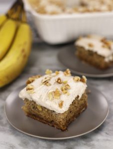 A slice of cake from Banana Sheet cake topped with a browned butter frosting and chopped walnuts.