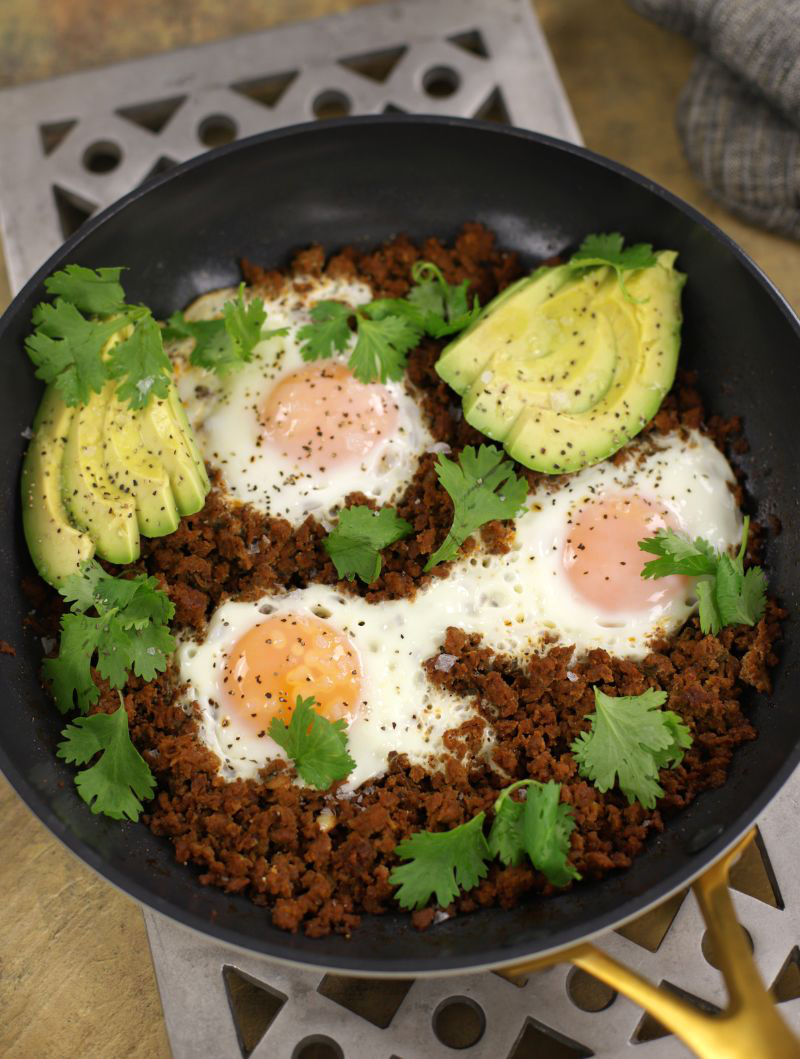 Chorizo and Eggs in a frying pan with avocado slices and fresh cilantro.