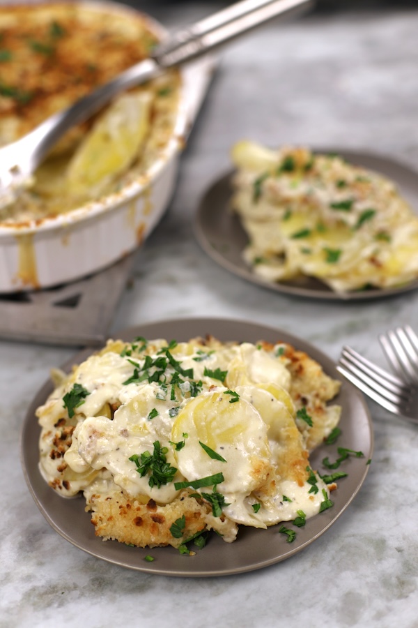 Scalloped Potatoes served on a small dark tan plate and garnished with parsley.