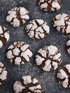 Chocolate Crinkle Cookies with crackled powdered sugar tops arranged on a dark baking sheet.