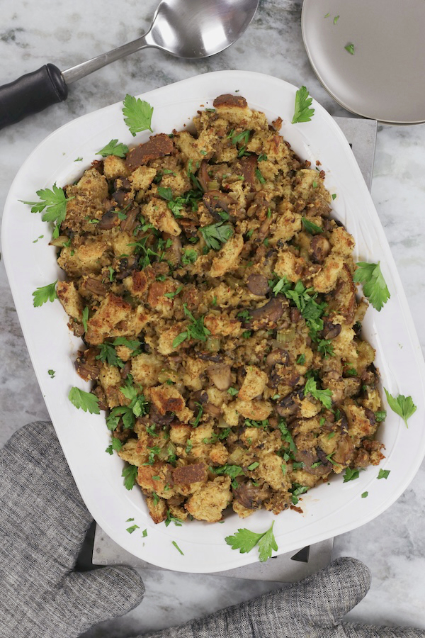 A white casserole dish of Sourdough Dressing that is garnished with Italian parsley.