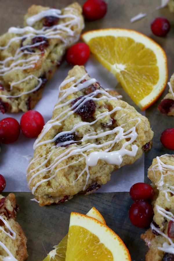 Orange and Cranberry Scones on a flat surface surrounded by orange slices and cranberries.