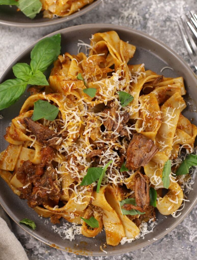 Close-up of Beef Ragu on wide pappardelle pasta, finished with fresh basil leaves and a sprinkle of parmesan.