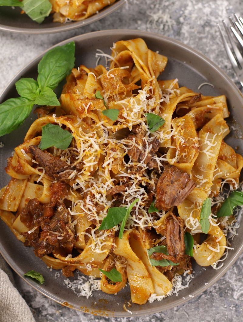 Close-up of Beef Ragu on wide pappardelle pasta, finished with fresh basil leaves and a sprinkle of parmesan.