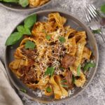 Slow-Cooked Beef Ragu on Pappardelle, served on a light brownish-grey plate atop a cement countertop.