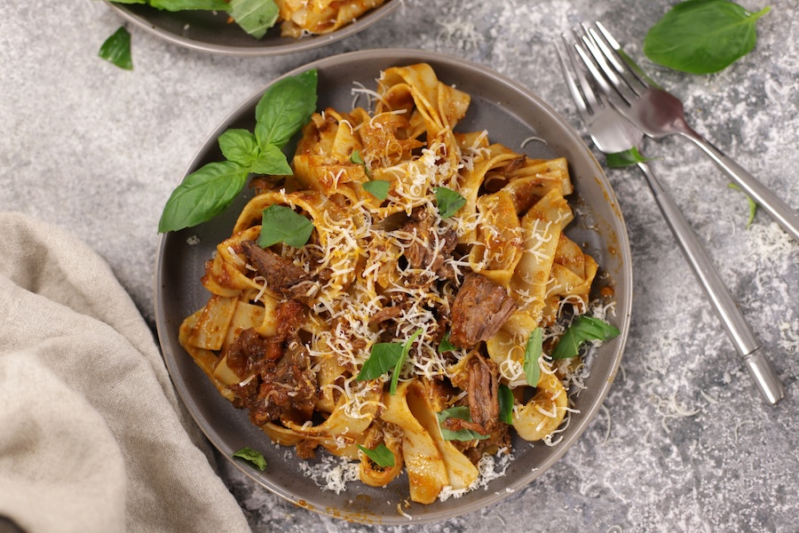 Slow-Cooked Beef Ragu on Pappardelle, served on a light brownish-grey plate atop a cement countertop.