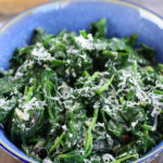 Overhead photo of Sautéed Spinach in a bowl sitting on a wooden table.