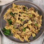 Overhead photo of Easy Ground Beef Stroganoff with mushrooms in a gray plate with a fork and a tan napkin sitting besides it.