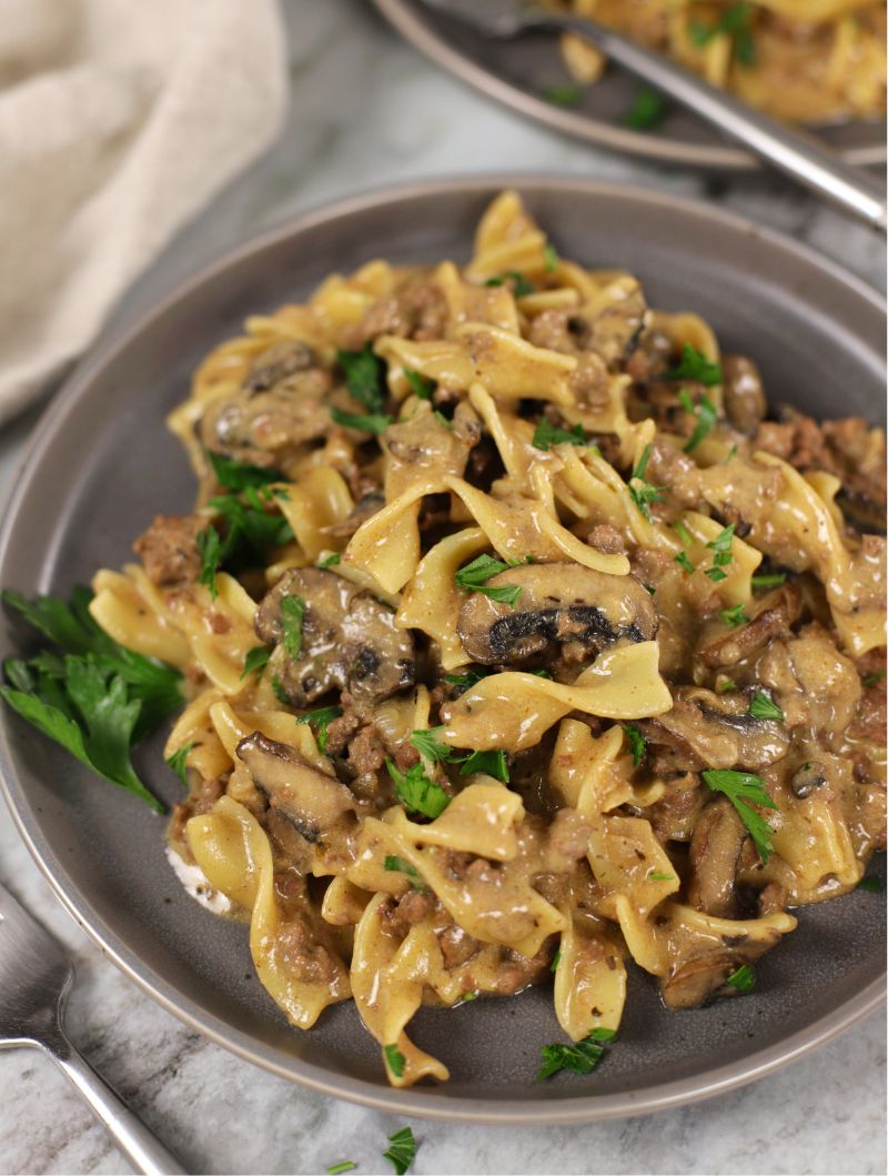 Ground Beef Stroganoff with mushrooms served on a gray plate that is sitting on a marble countertop with a napkin beside plate.
