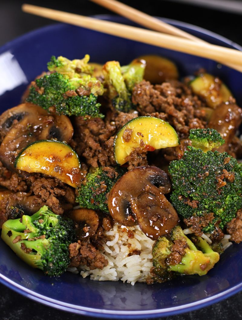 Ground Beef Teriyaki with zucchini, broccoli, mushrooms and rice served in a blue glass bowl with chopsticks on top.