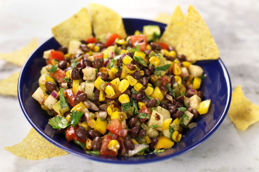 Black Bean Corn Jicama Salad served in a blue bowl with bright colors of yellow from the corn, red from the tomatoes and green from the jalapeños and cilantro.