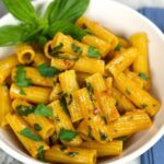 A bowl of Anchovy and Tomato Pasta tossed in a glossy golden sauce and garnished with fresh herbs.
