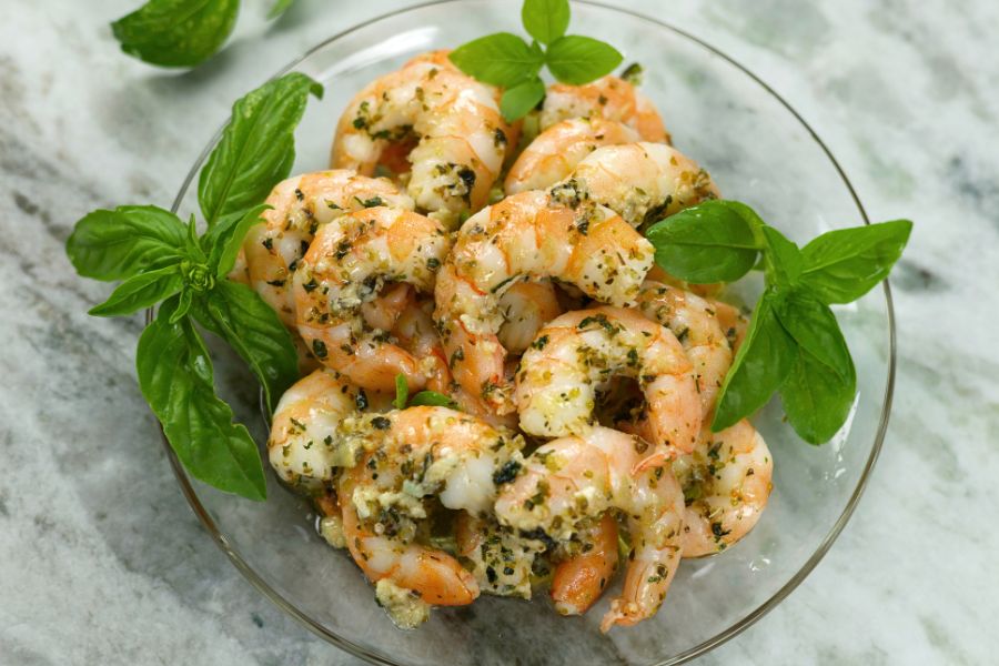 A bowl of juicy Baked Shrimp served on a glass plate sitting on a marble countertop.