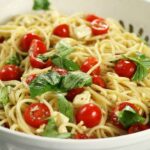 Mozzarella Spaghetti made with halved cherry tomatoes, fresh basil, lemon and olive oil served in a white pasta bowl.