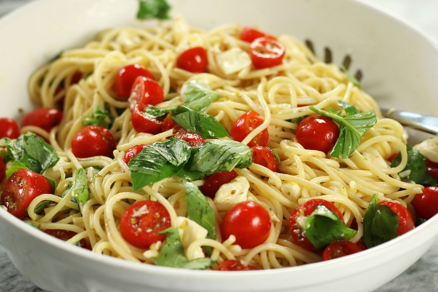 Mozzarella Spaghetti made with halved cherry tomatoes, fresh basil, lemon and olive oil served in a white pasta bowl.