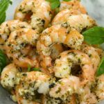 Oven Baked Shrimp coated with herbs piled on a clear glass plate.