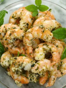Oven Baked Shrimp coated with herbs piled on a clear glass plate.