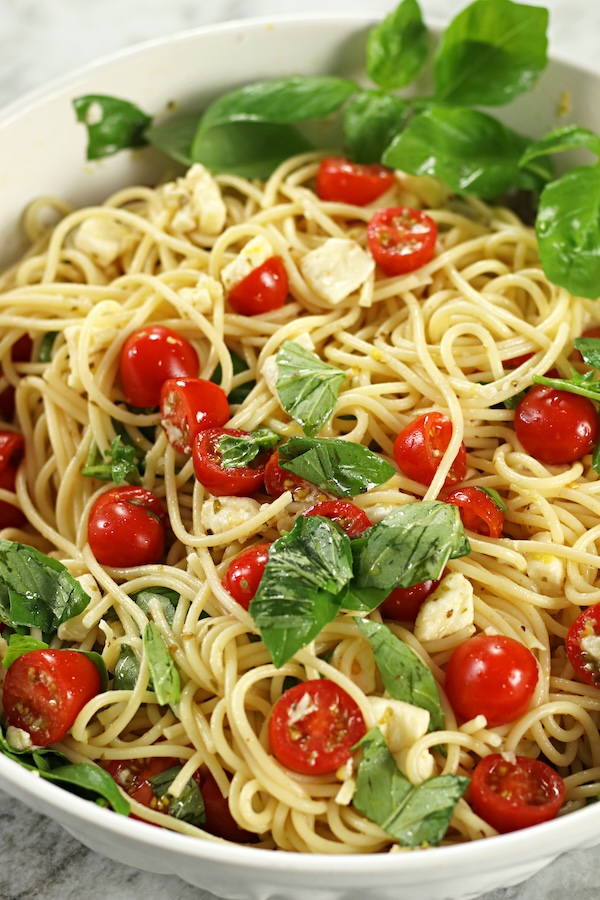 Easy no-cook Pasta with Mozzarella Cheese with cherry tomatoes, fresh basil and spaghetti served in a white bowl on a marble surface.