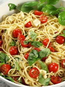 Tomato and Mozzarella Pasta in a white pasta bowl with fresh cherry tomatoes, mozzarella cubes and torn basil tossed with spaghetti.