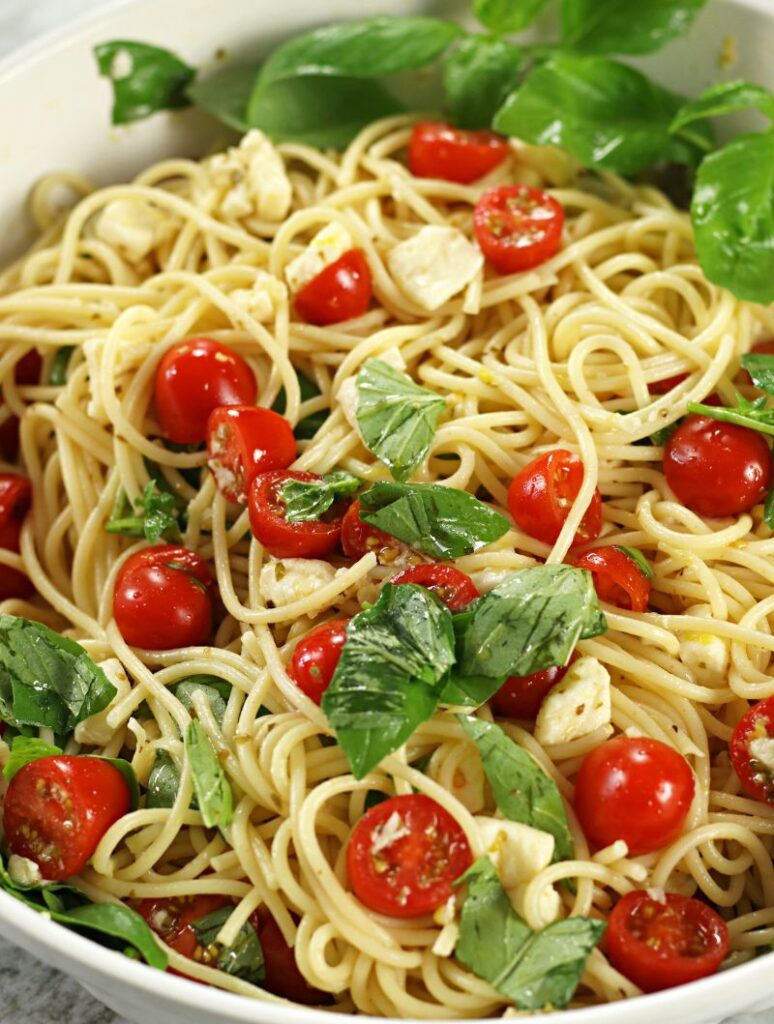 Tomato and Mozzarella Pasta in a white pasta bowl with fresh cherry tomatoes, mozzarella cubes and torn basil tossed with spaghetti.