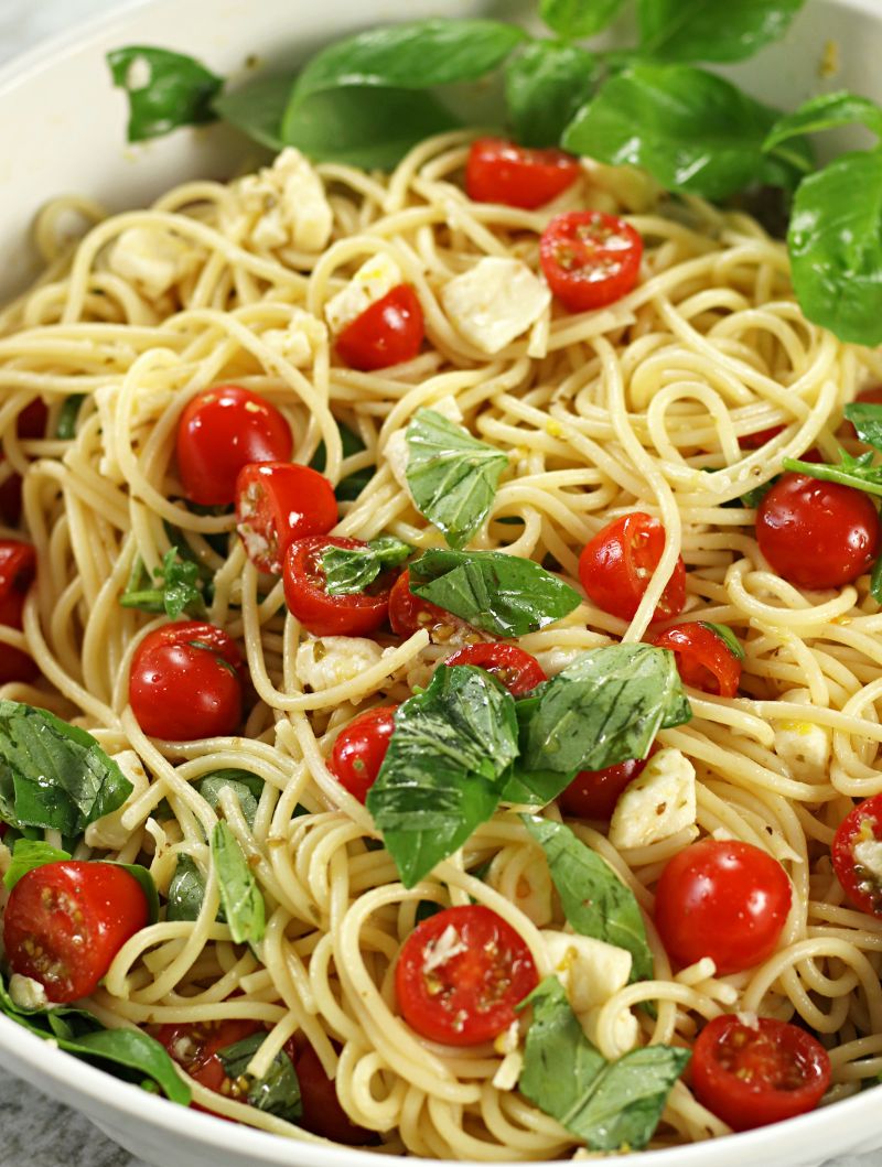 Tomato and Mozzarella Pasta in a white pasta bowl with fresh cherry tomatoes, mozzarella cubes and torn basil tossed with spaghetti.