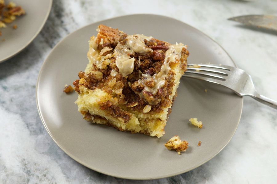 A slice of Almond Coffee Cake on a light brown plate, with a few crumbs scattered beside it.