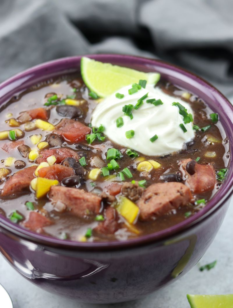 Close up of a bowl of Black Bean Soup with corn, tomatoes, sausage, and a lime wedge.
